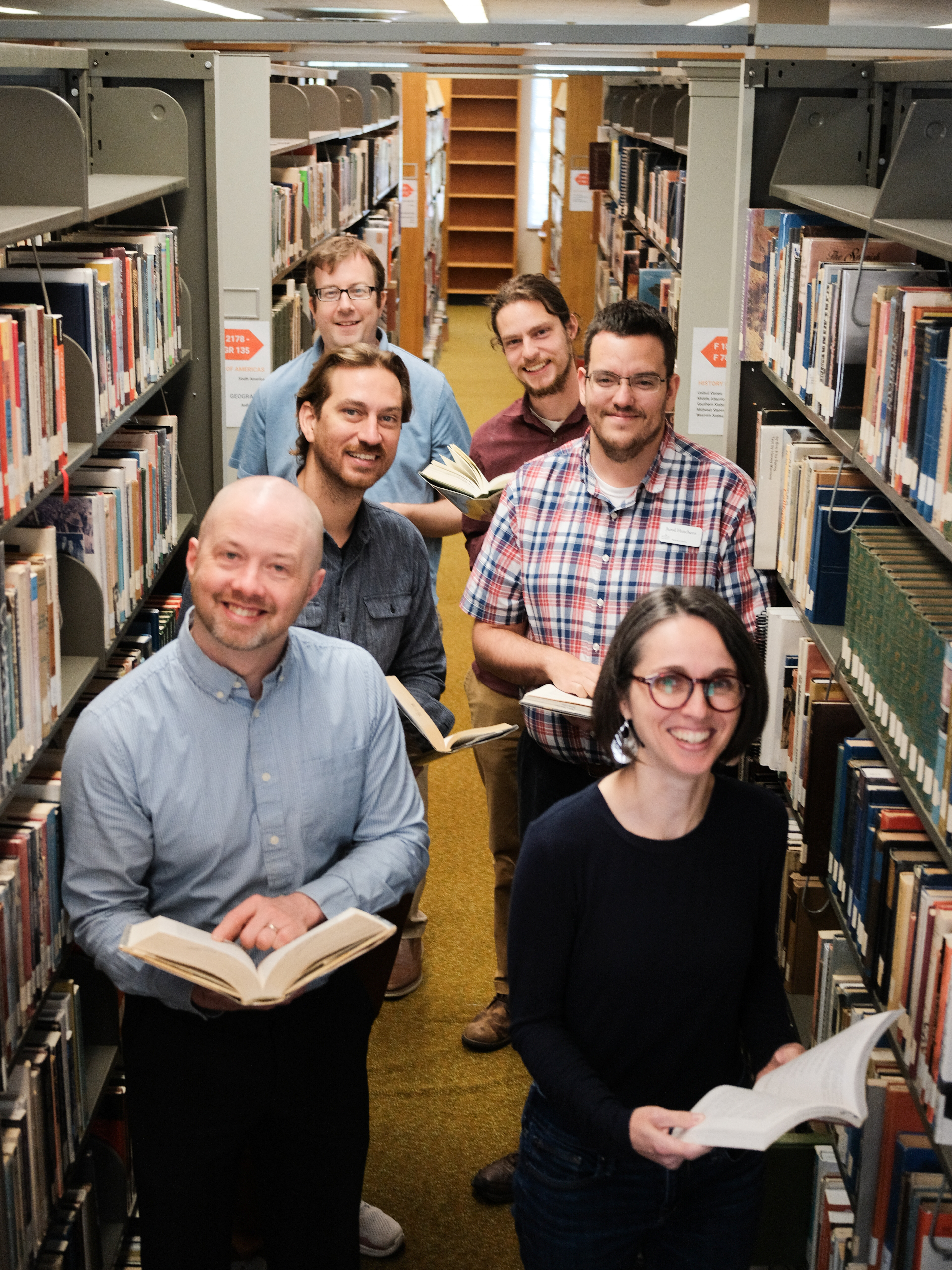 Library staff in between bookshelves holding books